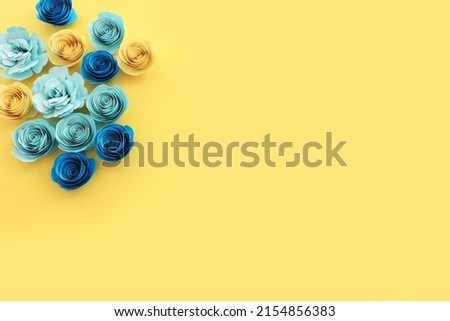 Top view image of paper flowers composition over yellow background