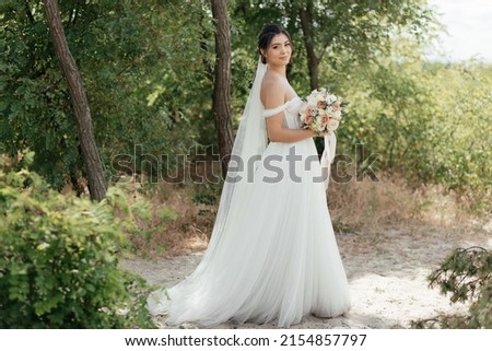  Portrait of a stunning bride posing with a bouquet in nature. High quality photo