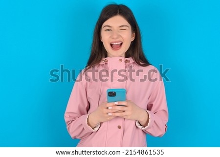 Young caucasian woman wearing pink raincoat over blue background taking a selfie  celebrating success