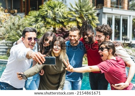 Group of mixed age range friends taking selfy in the garden of the villa with pool on holiday, people having fun on vacation, diversity and happiness concept