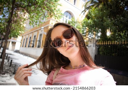 Beautiful young female tourist selfies poising for camera on a city street while traveling in summer. Happy traveler, tourist girl in sunglasses walking outdoors. Modern people lifestyle.