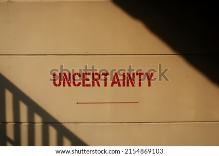 Wall with text inscription and direction sign UNCERTAINTY, means lack of certainty or sureness of event, inability to foretell outcomes to make predictions in future Royalty-Free Stock Photo #2154869103