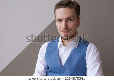 Trust and business concept Portrait successful young entrepreneur in blue vest white shirt smiling broadly with self-confident expression with beard looking at camera against background wall in office