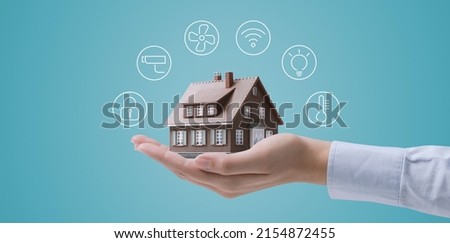Hands holding a miniature home model with icons, smart home automation concept