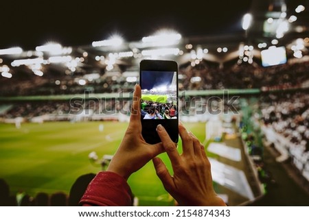 Fan hand with smartphone photographing football match. Using mobile phone camera at the stadium