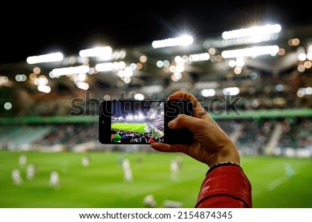 Using a smartphone camera for photographing a football match in the stadium.