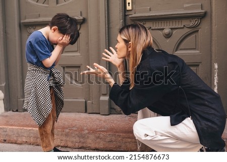 Mother scolds her son on the street. A child cries, a woman shakes her finger because of the boy bad behavior, while walking to home. Rule of conduct. Woman sitting, boy cover his face and cry. Royalty-Free Stock Photo #2154876673