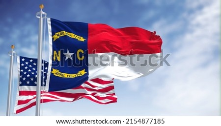 The North Carolina state flag waving along with the national flag of the United States of America. North Carolina is a state in the Southeastern region of the United States Royalty-Free Stock Photo #2154877185