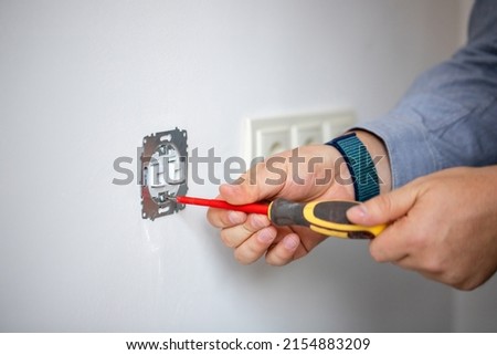 Man doing electrics. Close up of man installing electrical outlet in wall in room of house. Male electrician uses screwdriver to tighten bolts while attaching metal part of socket to wall. Royalty-Free Stock Photo #2154883209