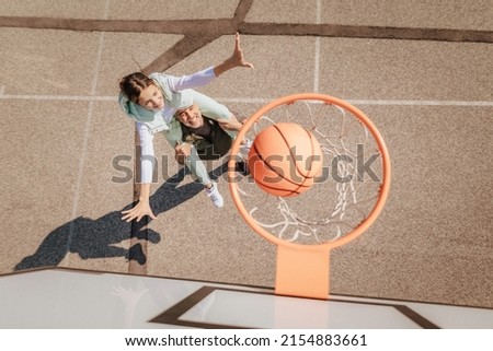 Father and teenage daughter playing basketball outside at court, high angle view above hoop net. Royalty-Free Stock Photo #2154883661