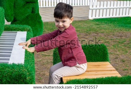 decorative piano covered with grass and kid pretending to play at keyboards. colorful flowers in the interior of the piano. beautiful easter decor outside, in a city capital. 