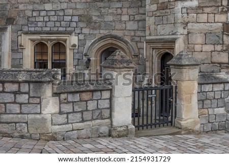 Private gateway onto a house made of old stone with a black wrought iron gate and an arched doorway and windows
