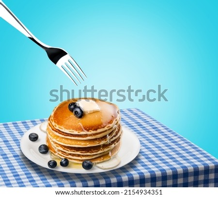 Fork with sweet pancakes in white plate on kitchen tablecloth.