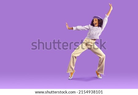 Overjoyed African American teen girl in fashionable clothes dance on violet studio background. Funny black teenage young woman have fun make dancer moves. Hobby and entertainment. Royalty-Free Stock Photo #2154938101