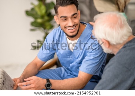 Young caretaker smiling at an elderly person sitting beside him Royalty-Free Stock Photo #2154952901