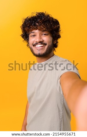 Selfie time. Joyful carefree Indian young curly man talking selfie, looking at the camera and smiles, recording stories on his phone, vertical portrait Royalty-Free Stock Photo #2154955671