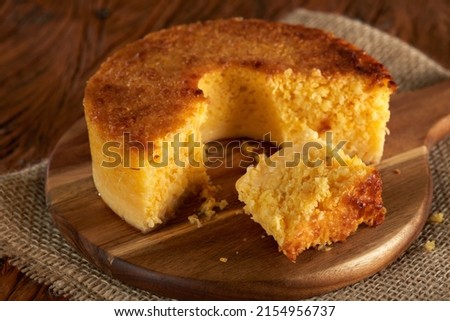 Homemade round cake made of green corn and cheese, known as "Pamonha Cake". Typical Brazilian food of Festa Junina(june festival) with a piece cut on a round wooden board on a rustic wooden table. Royalty-Free Stock Photo #2154956737