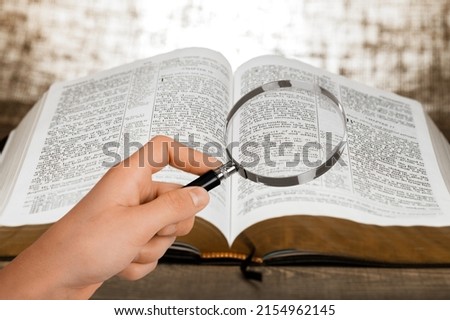 A magnifying glass in hand with open bible book. Royalty-Free Stock Photo #2154962145