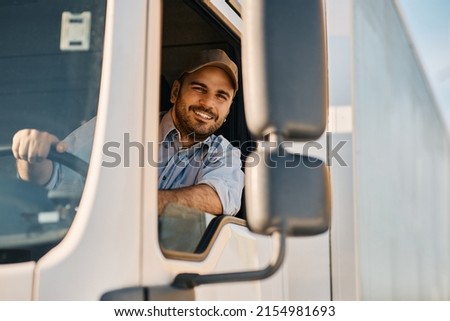 Happy professional truck driver driving his truck and looking at camera. Copy space. Royalty-Free Stock Photo #2154981693