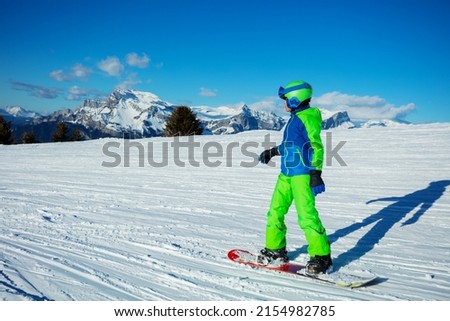 Side back view action photo of the boy on snowboard slide down the slope with Alps mountain peaks on background