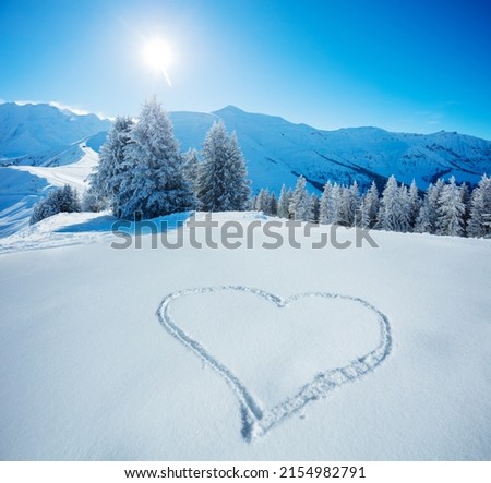 Heart symbol drawn in the snow on top of the mountain slope with snowy firs and range tops on background Royalty-Free Stock Photo #2154982791