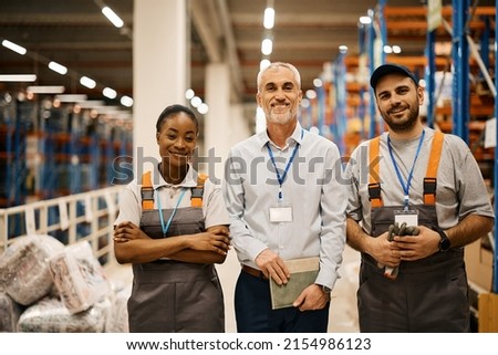 Portrait of young happy workers and their mature foreman at distribution warehouse looking at camera. Royalty-Free Stock Photo #2154986123
