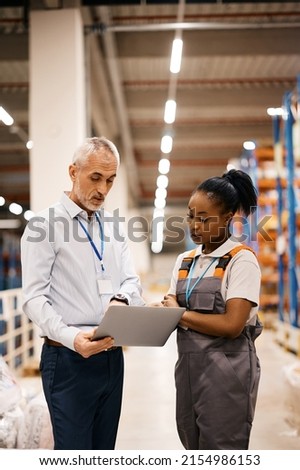 African American female worker and mature foreman using laptop while working at distribution warehouse.  Royalty-Free Stock Photo #2154986153