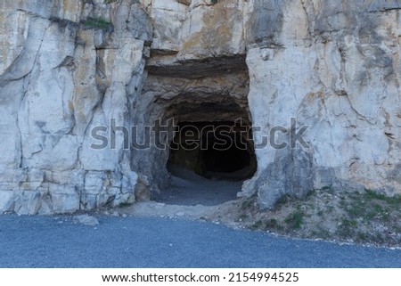 The concept of cave people's habitat. A stone wall with a dark hole, the entrance to the cave. Historical mineral mine. Royalty-Free Stock Photo #2154994525