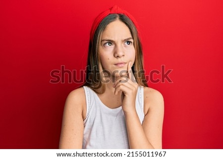 Beautiful brunette little girl wearing casual white t shirt thinking concentrated about doubt with finger on chin and looking up wondering 