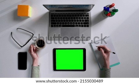 Top view of female hands writing notes using digital tablet with green screen at desk