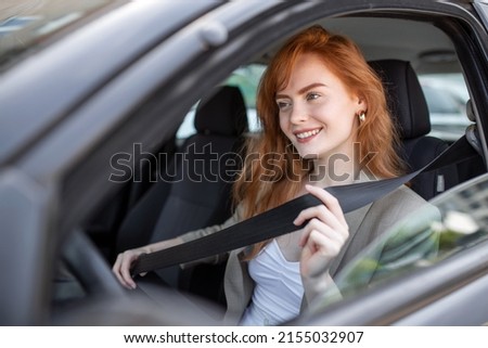 Young woman sitting on car seat and fastening seat belt, safety concept. Woman fastens a seat belt in the car. Caucasian woman driver fastening car seat belt while sitting behind the wheel car. Royalty-Free Stock Photo #2155032907