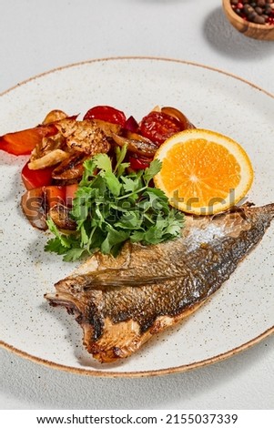 Fish dish - roasted dorado fillet with vegetables. Grilled fish fillet and roasted paprika, tomatoes and onion. Roast dorado fillet with garnish, greens and lemon on ceramic plate Royalty-Free Stock Photo #2155037339