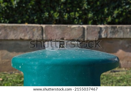 Picture shows  pair of dirty glasses placed on a green-blue bollard with a wall and bushes in the background