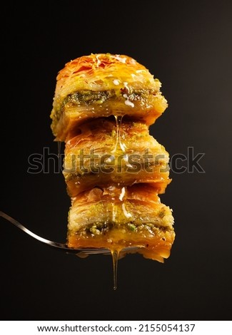 three delicious honey baklavas with pistachios on a fork on a black background, side view