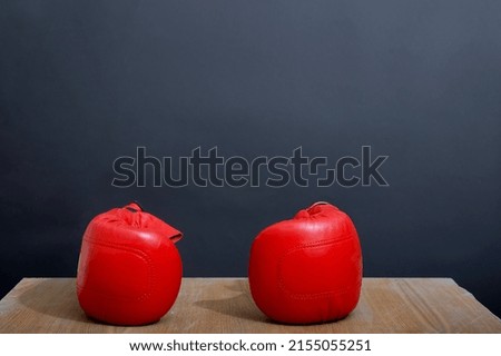 A set of two mild and comfortable red leather boxing gloves are on the light wooden table near a dark grey wall as a background, ready for competition