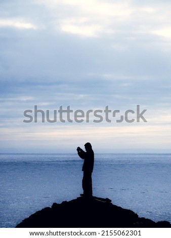 Man photographing the beach with the cell phone from a rock