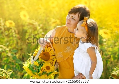 Happy grandmother and grandchild look towards copy space. Nature background. Senior woman holds basket of flowers and child in arms. Holidays and walks in fresh air at sunset. Happiness to be together