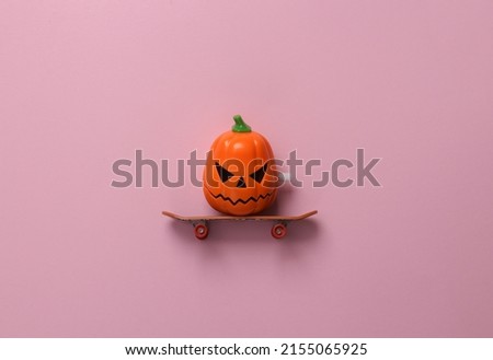 Jack o lantern on a skateboard on a pink pastel background. Minimal halloween still life