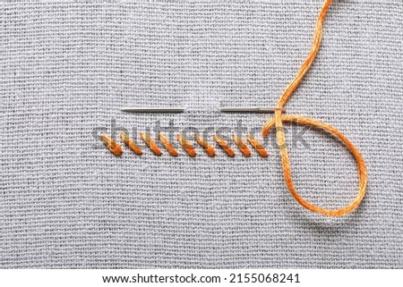 Needle with orange embroidery floss and row of stitches on grey fabric, top view Royalty-Free Stock Photo #2155068241