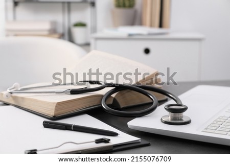 Open student textbook, clipboard and stethoscope near laptop on grey table indoors, closeup. Medical education