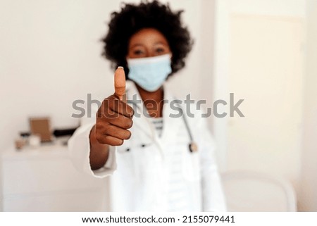 Portrait of a young doctor wearing a face mask and showing thumbs up in a hospital. Cropped shot of a young African-American female doctor showing thumbs up in her office.