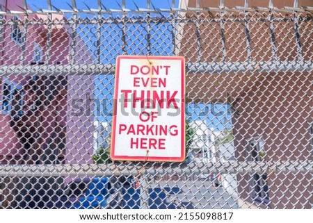 Don't even think of parking here signage on a metal mesh fence in San Francisco, California