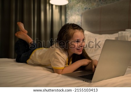 8 years old child having fun using laptop at her bedroom. High quality photo