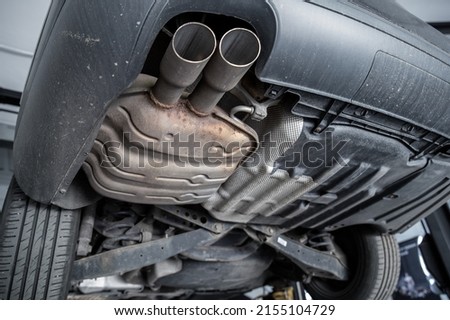 Close-up detail bottom view of car part metal exhaust muffler pipe with rusty stains. Lifted vehicle check-up maintenace service, repair and fix at automotive workshop Royalty-Free Stock Photo #2155104729