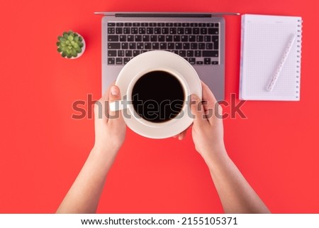 Top view photo of notebook, grey laptop with holding hands cup of black coffee on isolated red background. coffee break concept