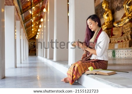 Asian buddhist woman reading Lanna Sanskrit ancient palm leaf manuscript of Tripitaka the Lord Buddha dhamma teaching while sitting in temple on holy full moon day to chant and worship in monastery Royalty-Free Stock Photo #2155122723