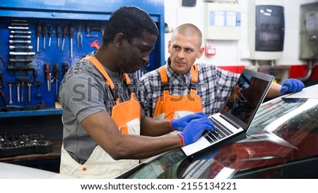 Two auto mechanics diagnosing car engine with laptop with special program at the car repair service center