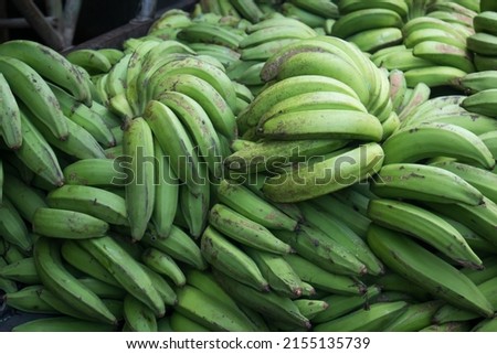a large pile of unripe bananas in a traditional market