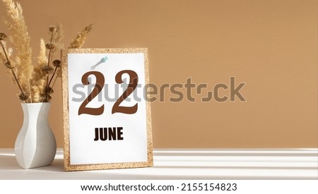 june 22. 22th day of month, calendar date.White vase with dead wood next to cork board with numbers. White-beige background with striped shadow. Concept of day of year, time planner, summer month.