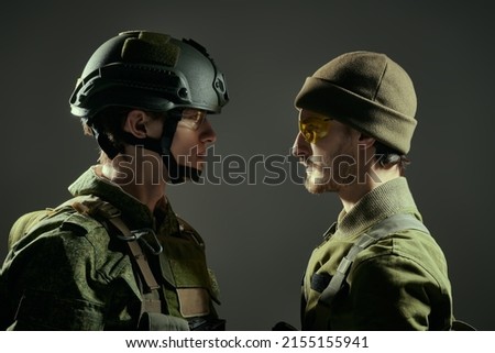 Military conflict. Two brave soldiers in Protective Combat Uniform stand face-to-face looking seriously at each other. Dark background. War concept.  Royalty-Free Stock Photo #2155155941